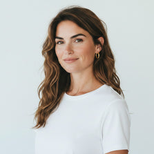 TYS Jewelers 10K yellow gold hoop earrings worn by a woman with wavy brown hair in a white t-shirt