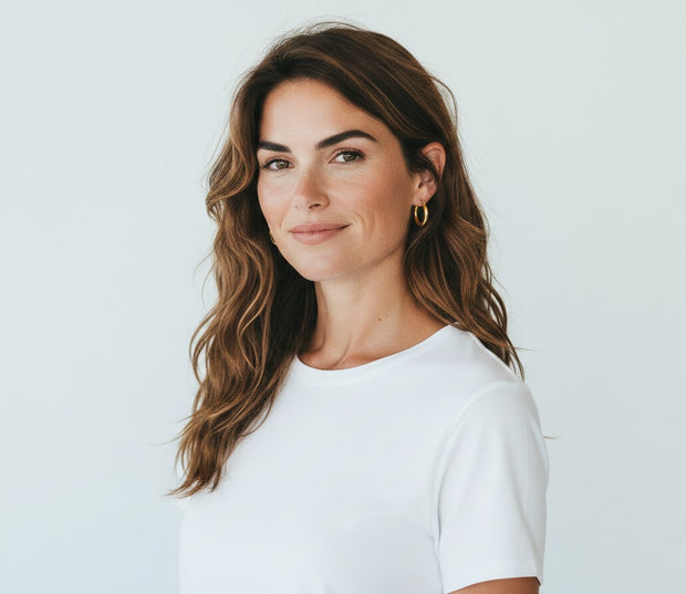 TYS Jewelers 10K yellow gold hoop earrings worn by a woman with wavy brown hair in a white t-shirt